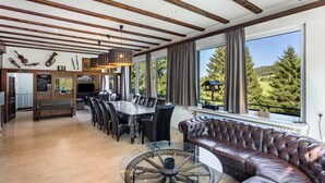 A spacious dining area with a large table and chairs, a leather sofa, and a view of a forested landscape.