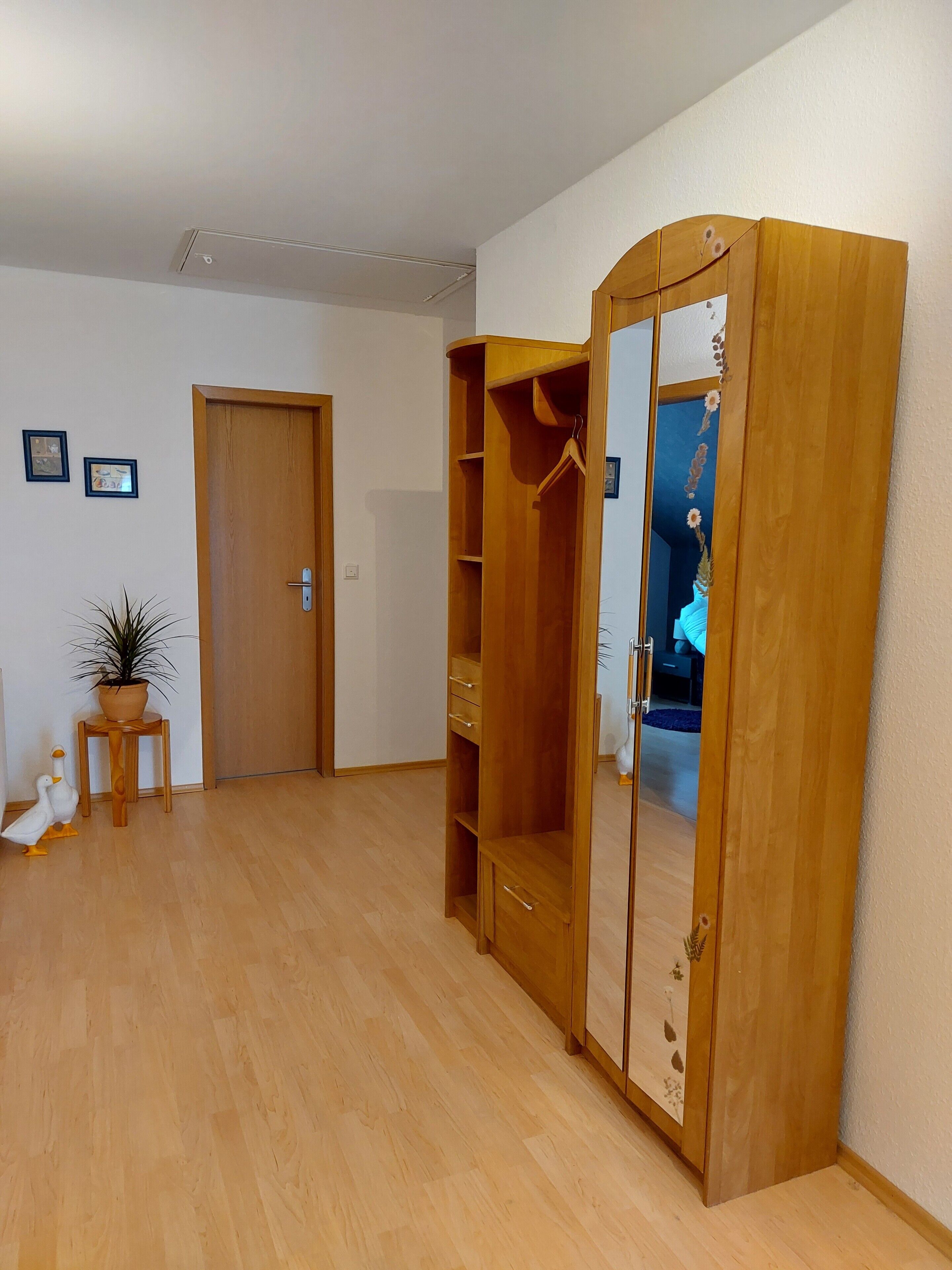 Ein Zimmer mit einem Holzschrank, einer Tür, einem kleinen Tisch mit einer Pflanze und einer Entenfigur.