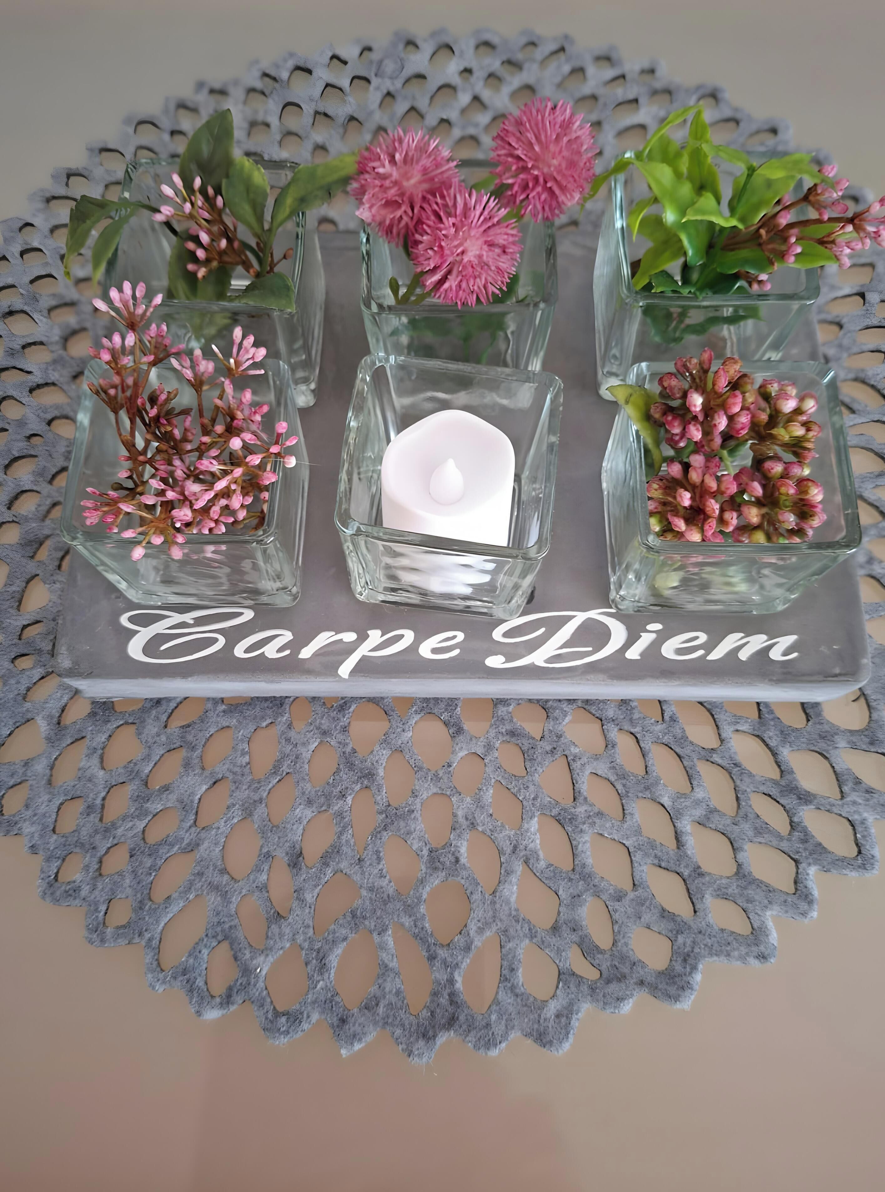 A tray with square glass vases containing pink flowers and a lit candle, labeled 'Carpe Diem.'