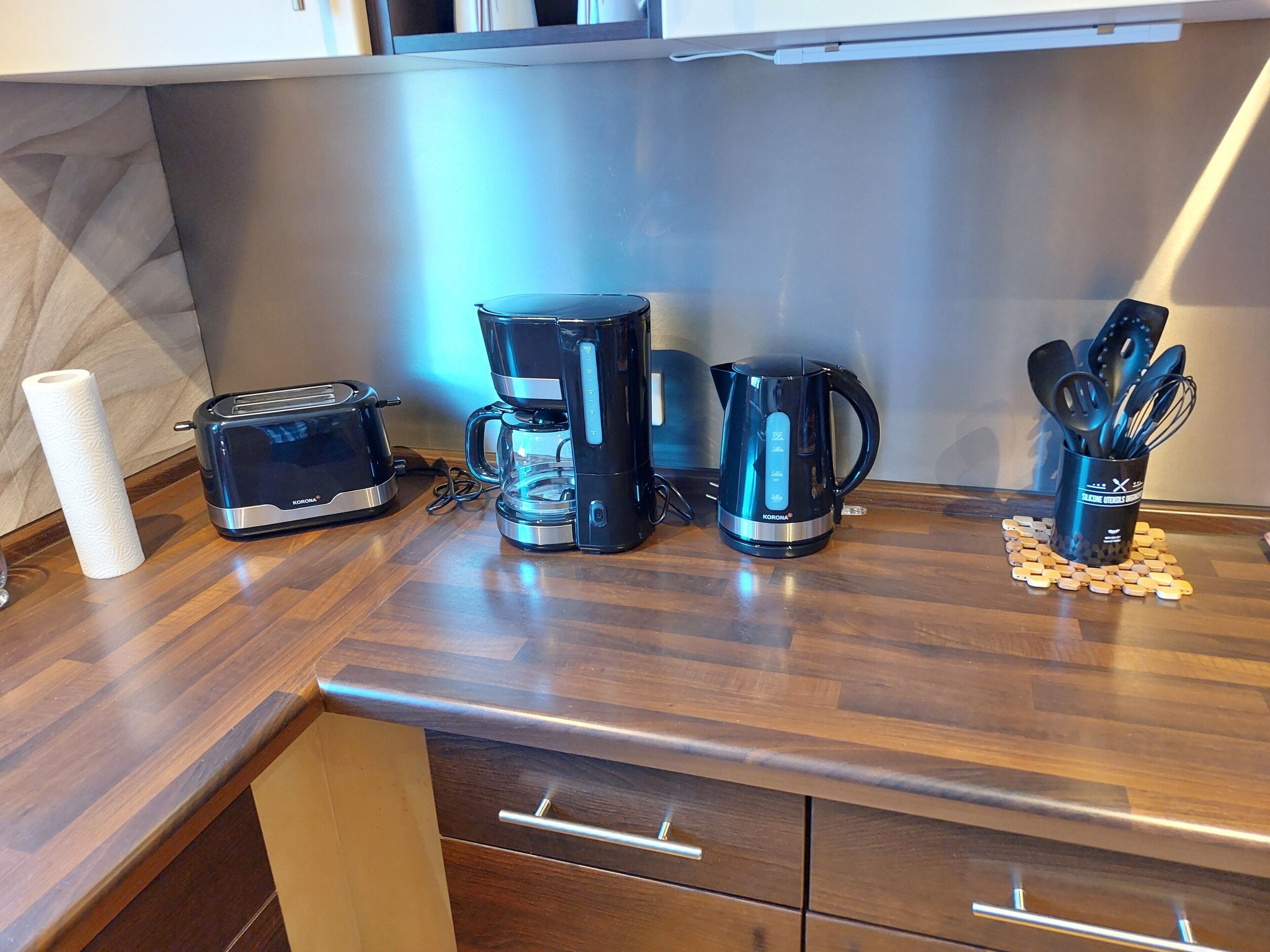 A kitchen counter with a toaster, coffee maker, and kettle, along with a utensil holder.