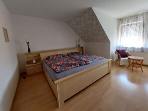 A bedroom with a wooden bed, a small table, a chair, and a window with curtains. - Apartment 'Lipperland' with Balcony and Wi-Fi (Detmold)