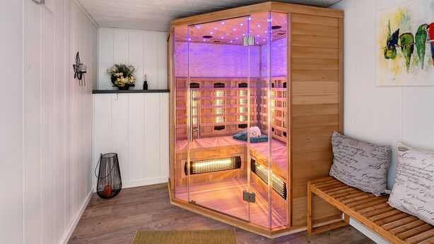 Una habitación con sauna de paredes de vidrio, banca de madera y estante empotrado con objetos decorativos.