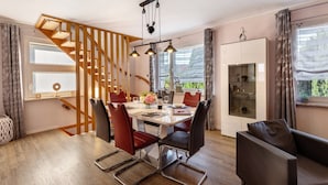 Un comedor con una escalera de madera, una mesa de comedor con sillas, una lámpara de araña y un aparador con puertas de cristal.
