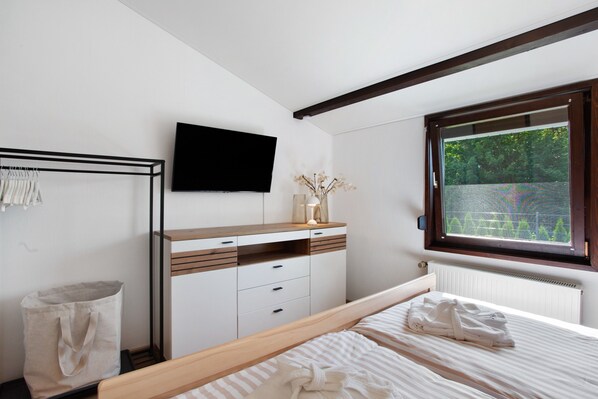 Un dormitorio con cama, cómoda, televisor, ventana y radiador.
