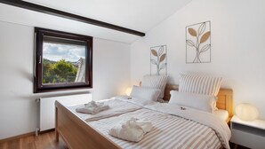 A modern bedroom with a large window, a bed with striped bedding, and two wall art pieces.