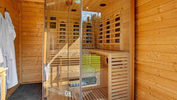 A wooden sauna room with glass doors, a bench, and a towel rack.