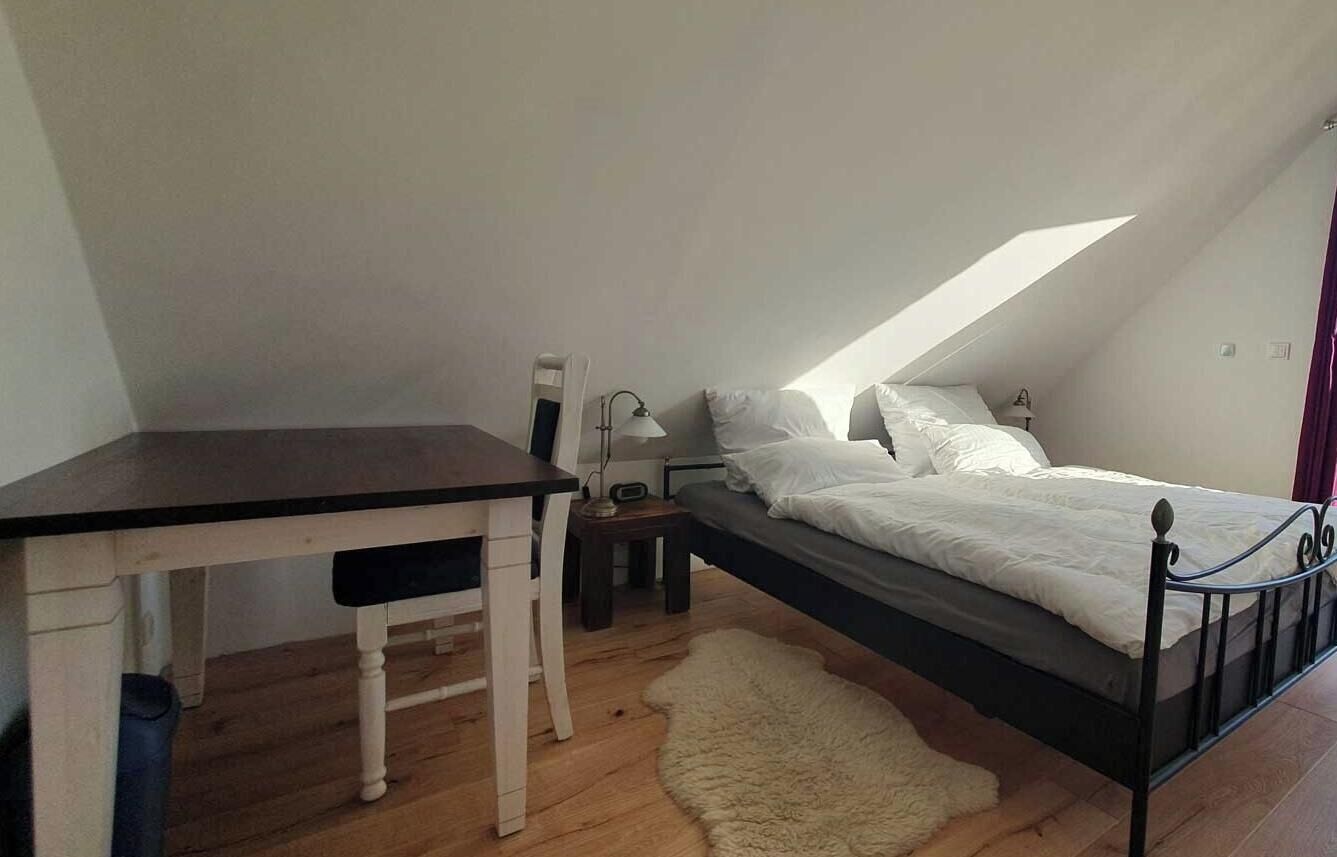 Een slaapkamer met een bed, een bureau, een stoel, een lamp en een klein vloerkleed.