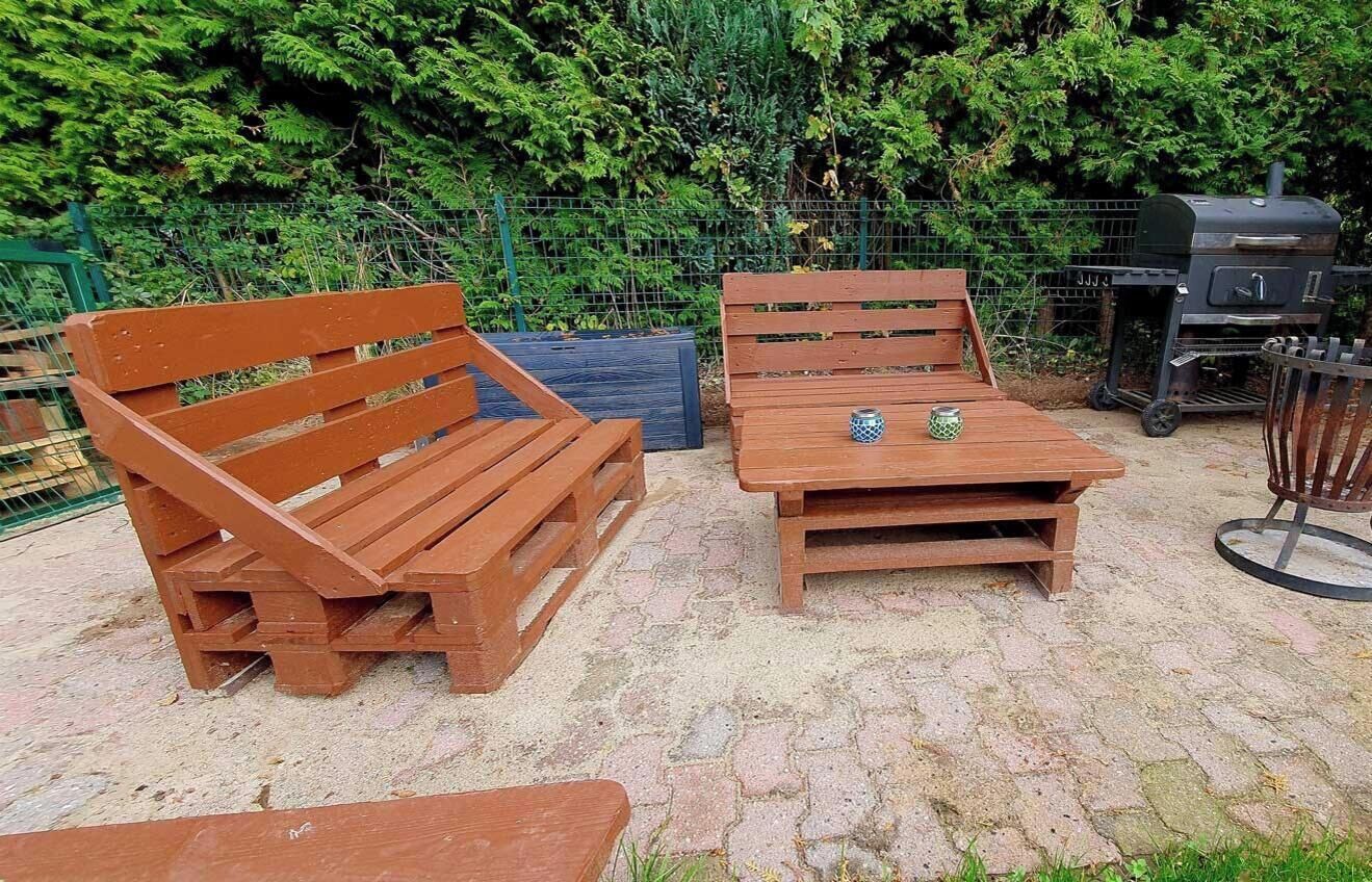 A wooden bench and table set outdoors with a grill in the background.