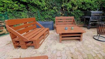 A wooden bench and table set outdoors with a grill in the background.
