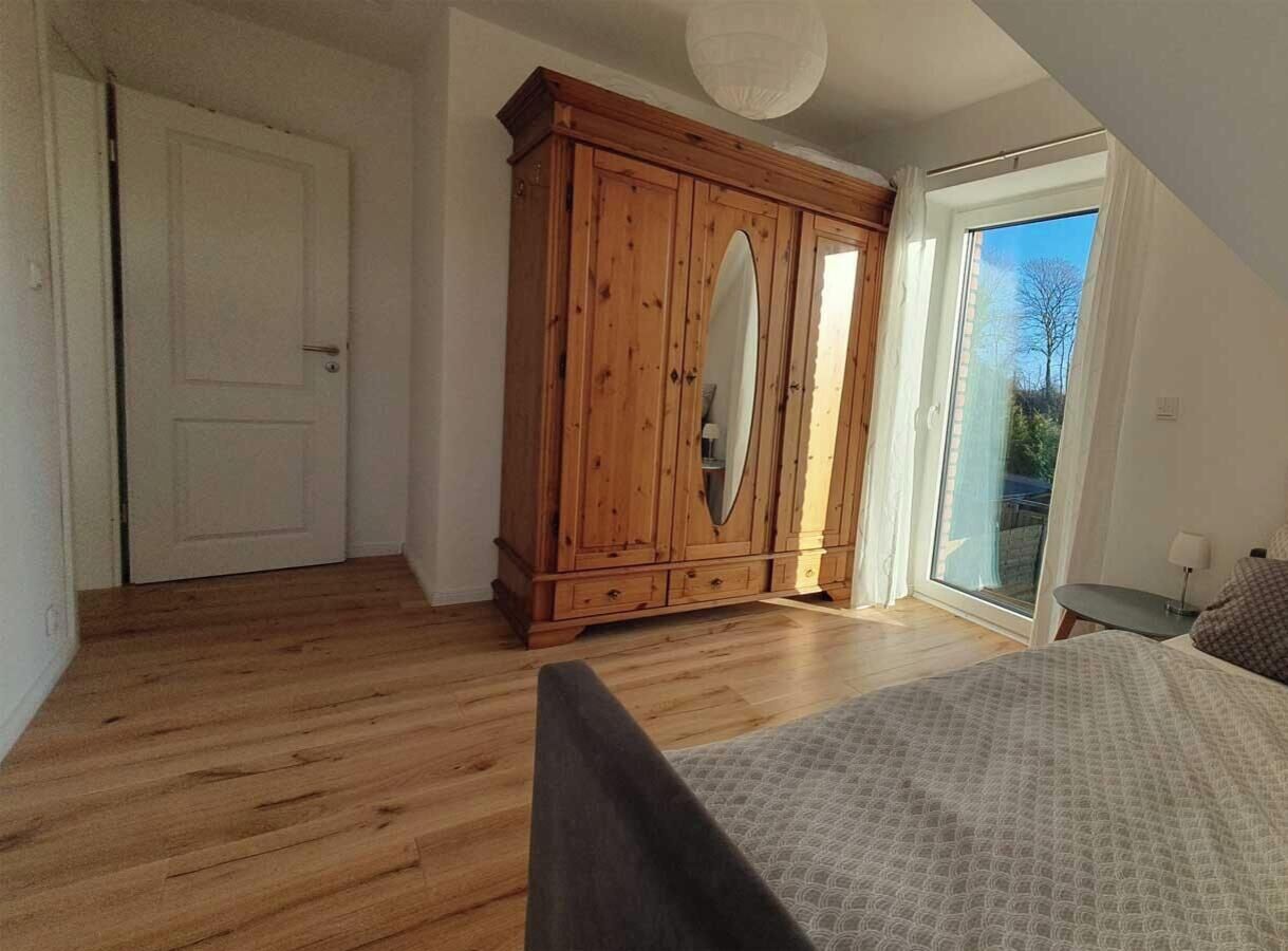 Ein Schlafzimmer mit einem Holfach, einem Bett, einem kleinen Tisch und Blick durch ein großes Fenster.