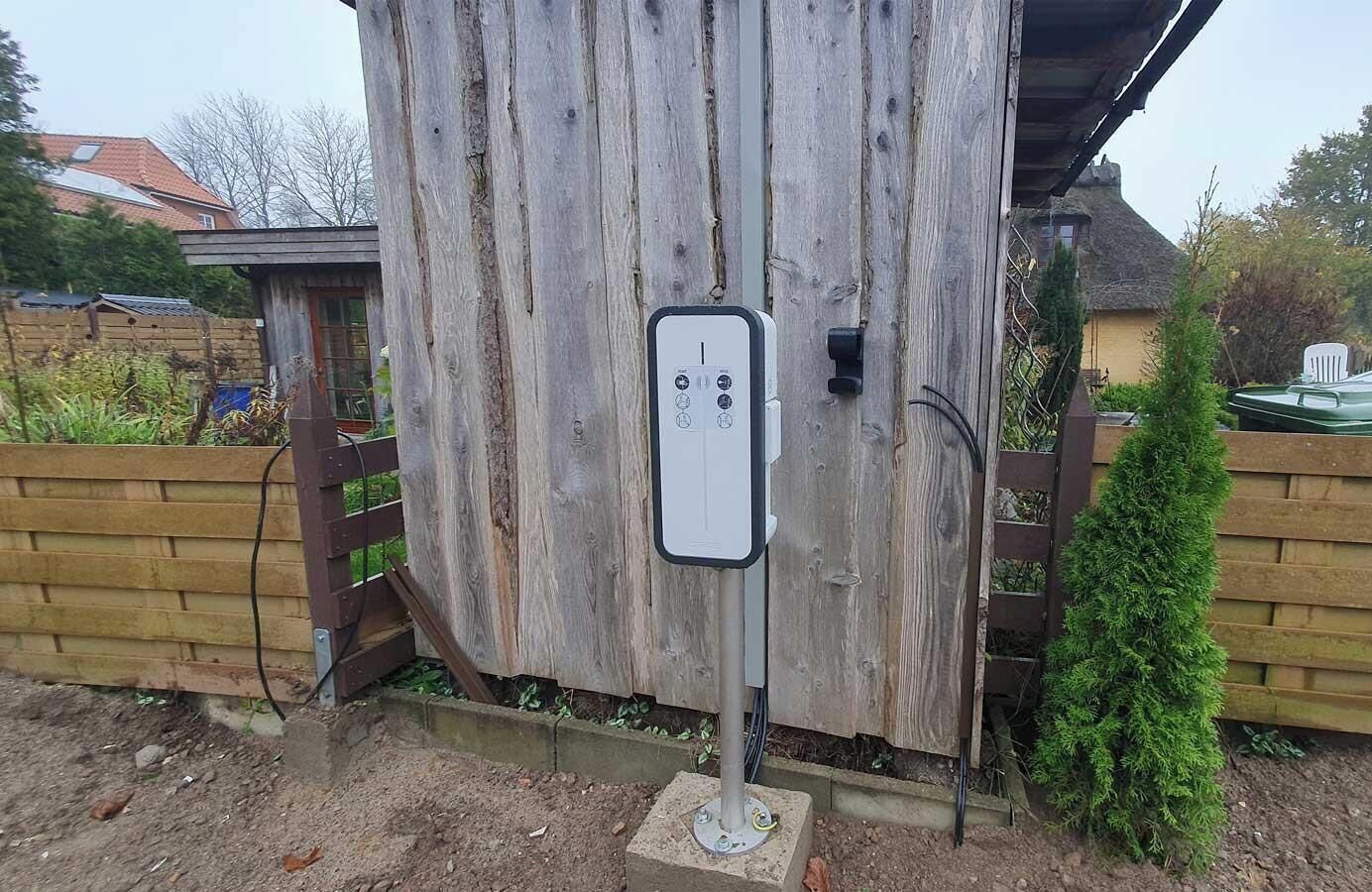 A wooden utility box with a white electrical panel, surrounded by a wooden fence and a small green shrub.