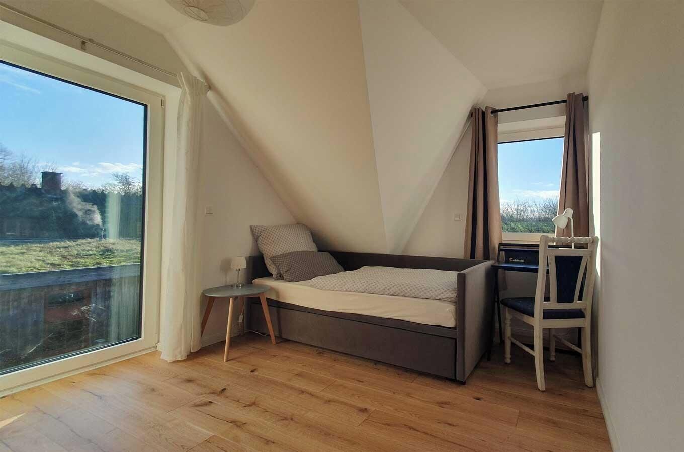 A loft bedroom with a bed, a small table, a chair, and a large window.