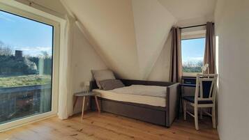 A loft bedroom with a bed, a small table, a chair, and a large window.