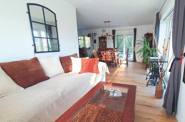 A living room with a sofa, coffee table, dining table, chairs, and a large window.