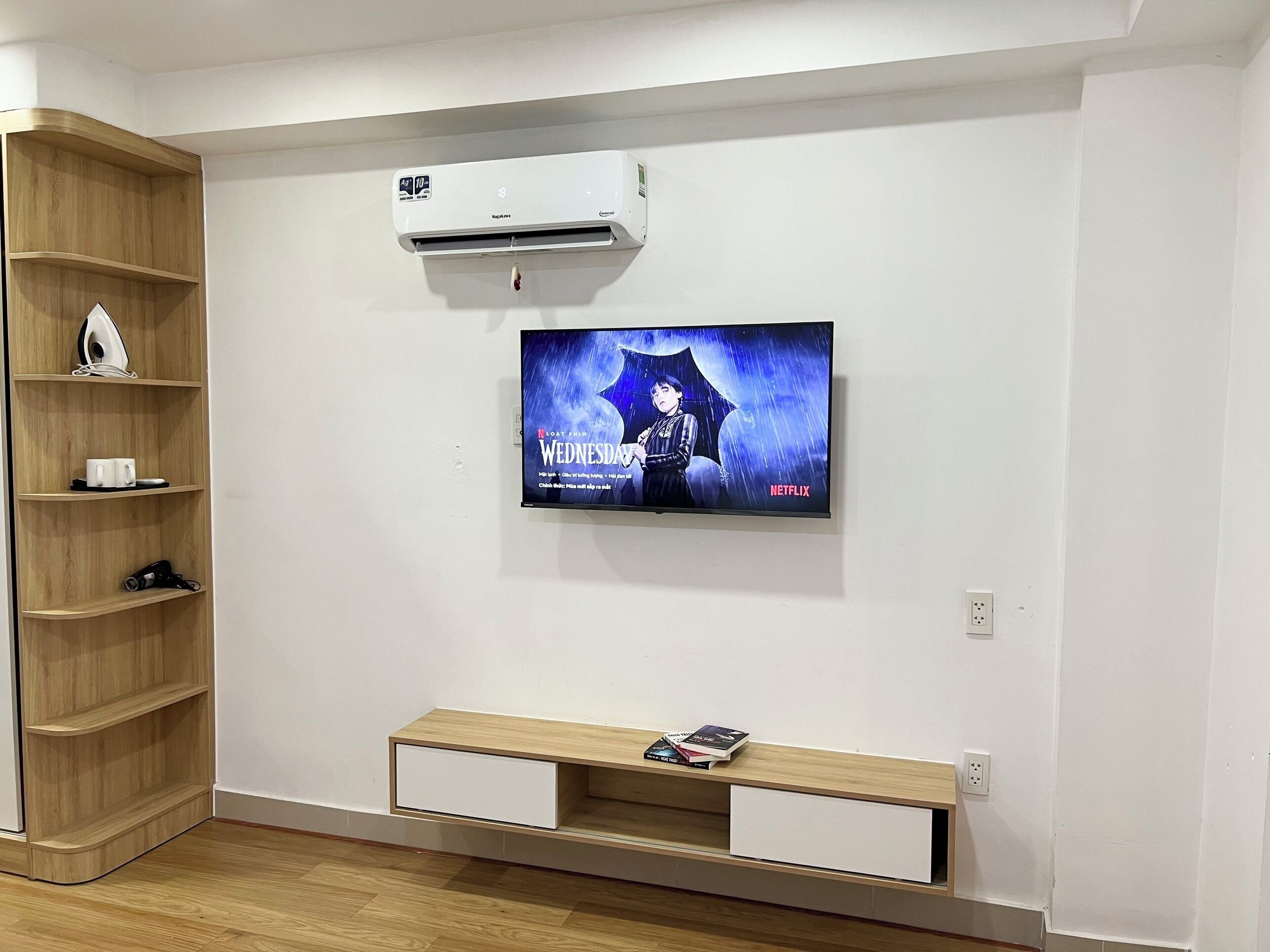 Un salon moderne doté d’un téléviseur à écran plat fixé au mur, d’une étagère en bois, d’un banc intégré avec espace de rangement et d’un climatiseur mural.