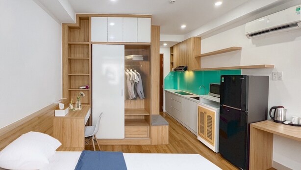 A modern hotel room with a bed, a desk, a kitchenette, and a walk-in closet.