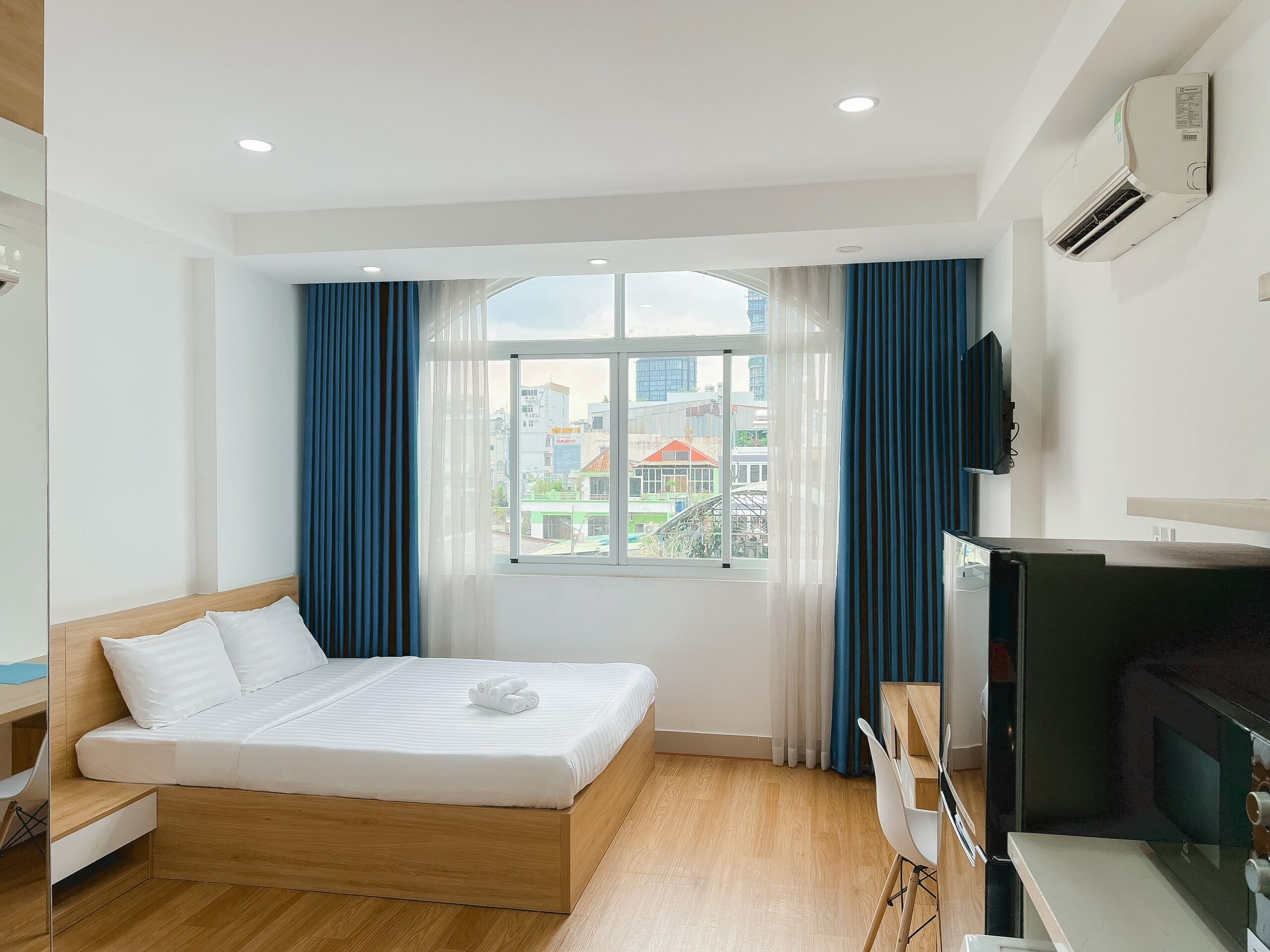 A modern hotel room with a bed, a desk, a TV, and a window with curtains.