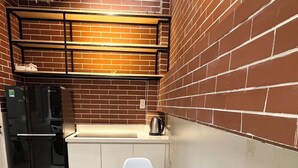 A compact kitchen with a white table and chairs, a black refrigerator, and a kettle on the counter.