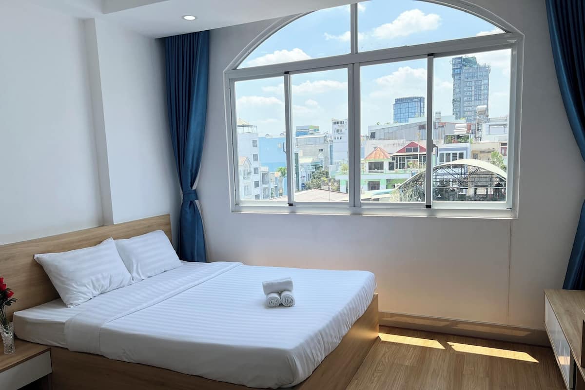 Quarto de hotel com uma cama, janela e cortina, e vista para a cidade.