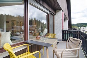 A balcony with a table, chairs, and a view of a forested area.
