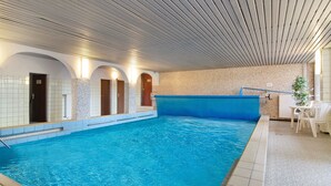 An indoor swimming pool with tiled walls, a wooden ceiling, and a seating area with chairs.