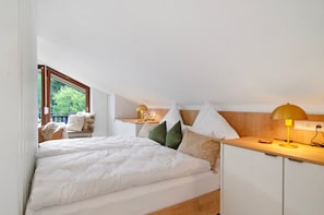 Une chambre à coucher avec un lit, des oreillers, une table de chevet, une lampe, une fenêtre et une vue sur la verdure.