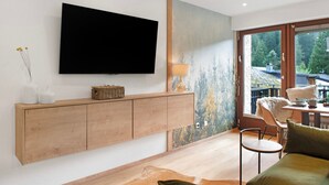 A modern living room with a flat-screen TV, wooden cabinet, and a large window with a view of trees.