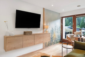 Un salon moderne doté d’un téléviseur à écran plat, d’un meuble en bois et d’une grande fenêtre donnant sur la verdure.