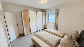 Une chambre à coucher comprenant un lit, deux tables de chevet, une armoire et une fenêtre avec des rideaux.