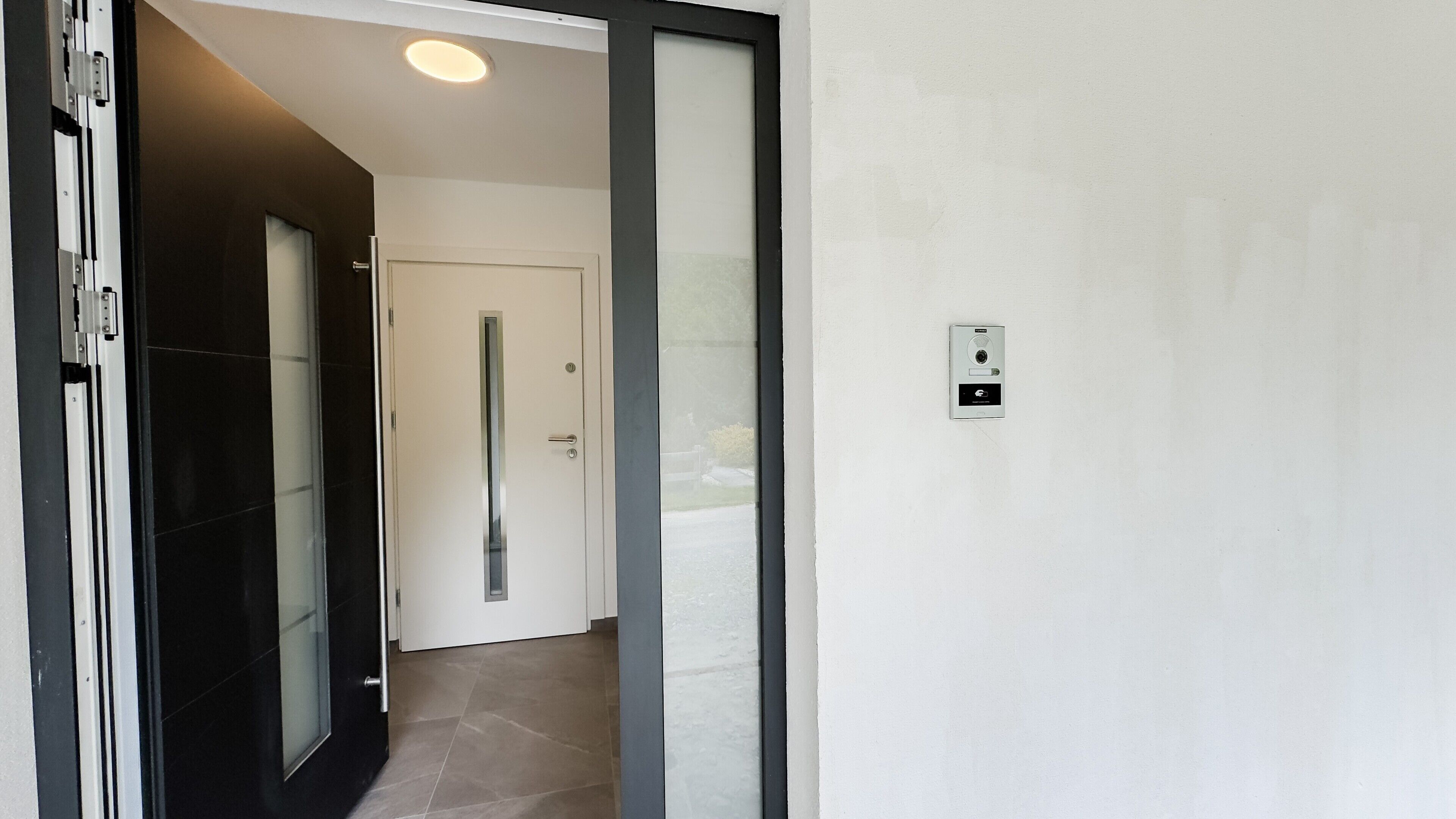 Een modern interieur met een schuifdeur, een deur met een handgreep en een intercom bevestigd aan de muur.