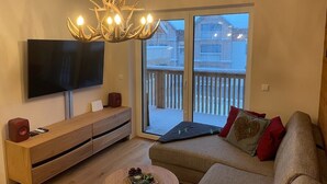 Een woonkamer met een televisie, een houten tv-meubel, een bank en een kroonluchter.
