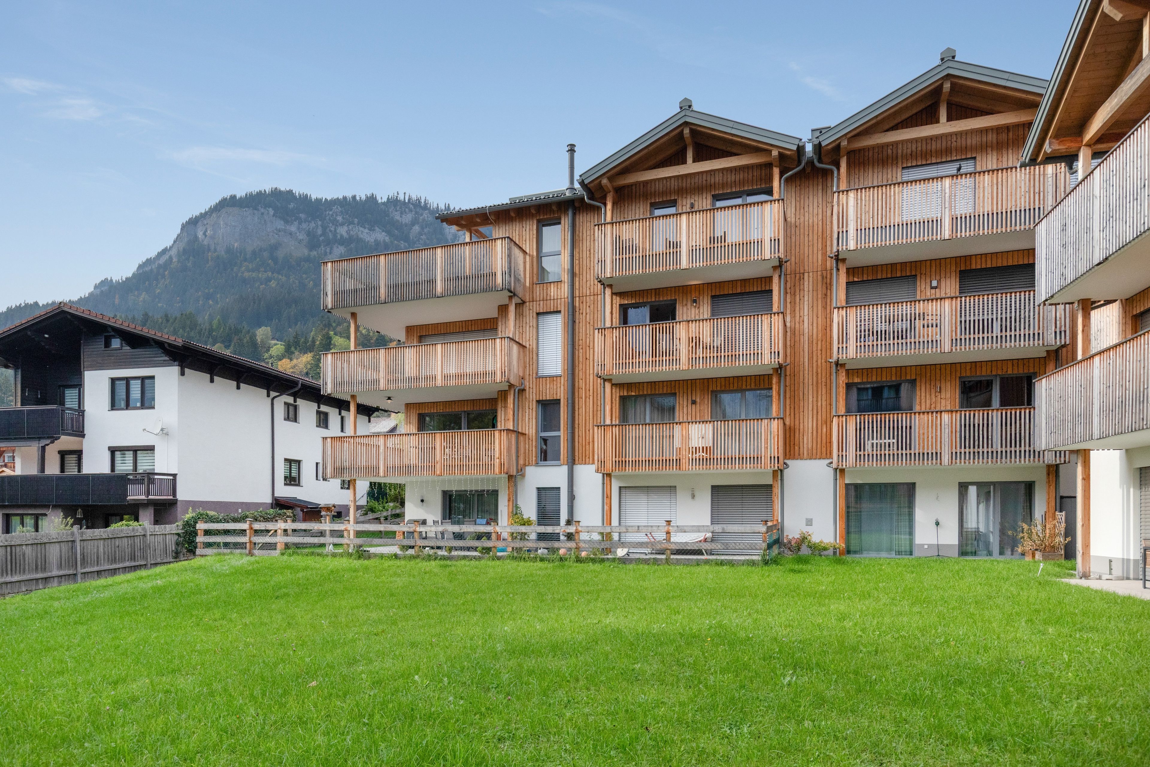 A multi-story building with balconies, a grassy courtyard, and a mountain in the background.