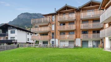 A multi-story building with balconies, a grassy courtyard, and a mountain in the background.