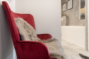 Ein roter Sessel mit einem Fellüberwurf, vor einer weißen Wand mit Fliesenboden.