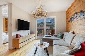 Een moderne woonkamer met een flatscreen televisie, een houten tv-meubel, een bank, een salontafel en een kroonluchter.