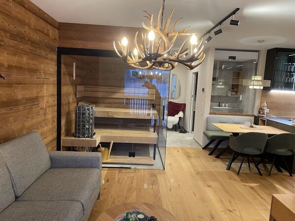 Un salon moderne avec un mur en bois, une cloison en verre, un coin repas comprenant une table et des chaises, et un lustre original en forme de bois de cerf.