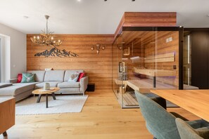 A modern living room with a wooden floor, a sofa, a coffee table, and a dining area with a glass partition.