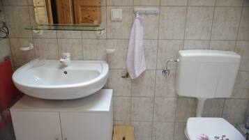 Ein Badezimmer mit einem weißen Waschbecken, einer Toilette und einem Glasregal darüber.