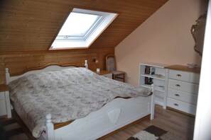 A bedroom with a sloped ceiling, a skylight, a bed with a floral bedspread, a nightstand, a dresser with drawers, and a mirror.