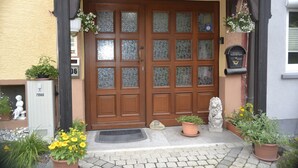 Eine doppelte Holztür mit Glasschildern, ein Briefkasten und Topfpflanzen an der Veranda.