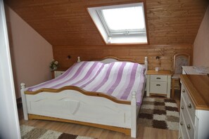 Een slaapkamer met een schuine plafond, dakraam, bed met gestreept beddegoed, nachtkastje, dressoir en stoel.