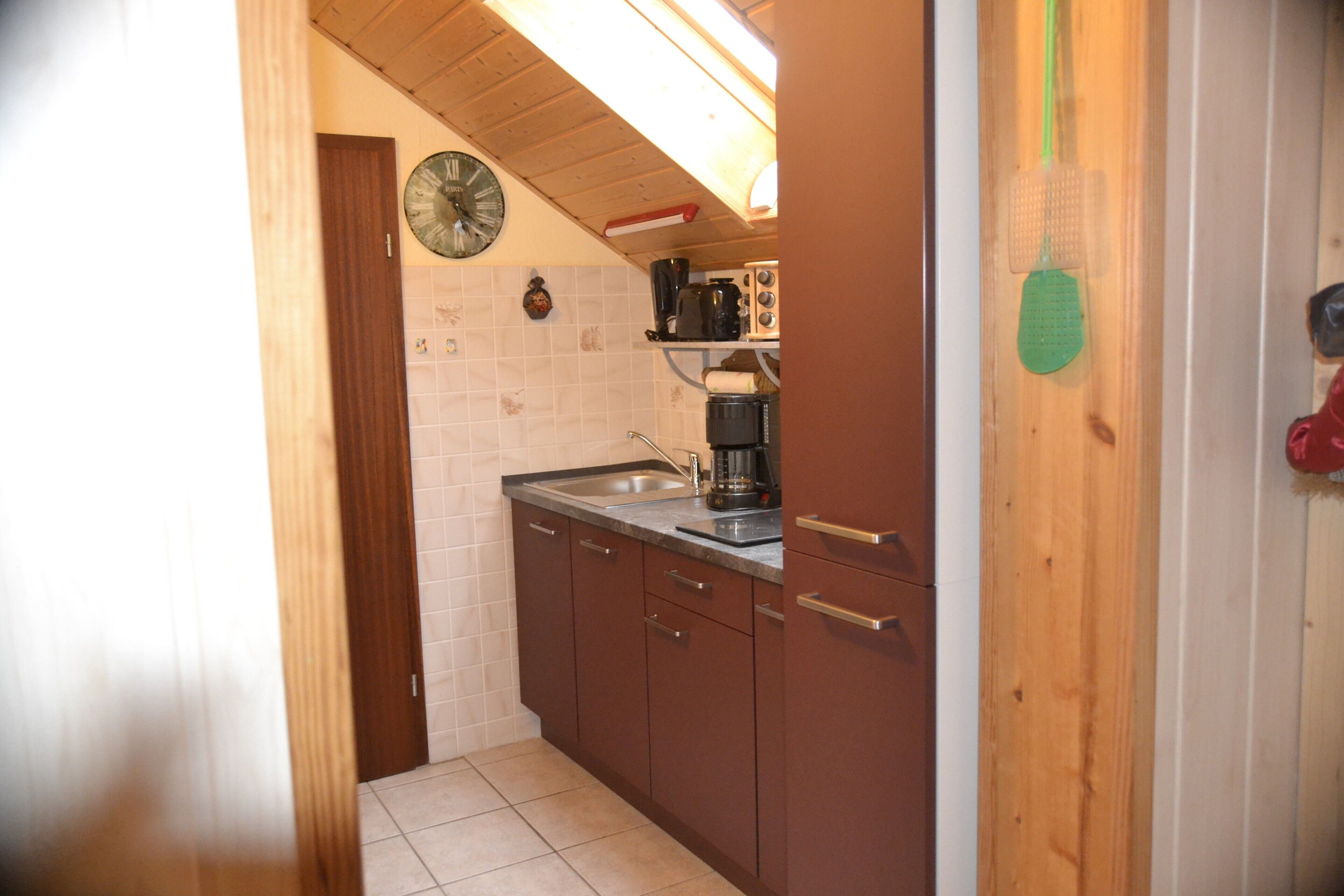 A kitchen with wooden cabinets, a sink, a clock, and a coffee maker.