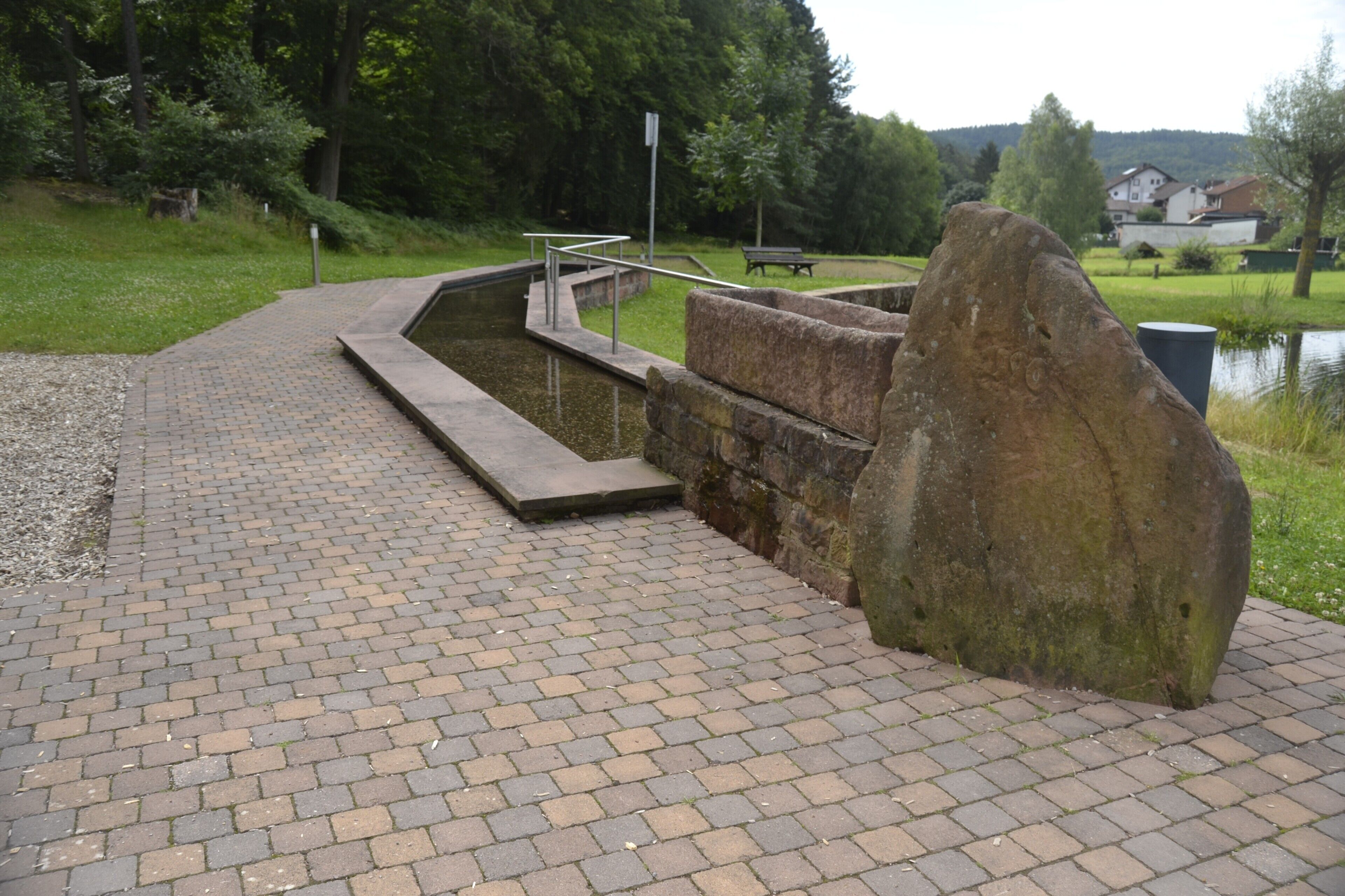 A paved walkway with a stone structure, a metal railing, and a large rock.