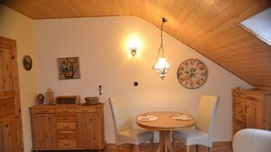 Ein Essbereich mit Holztisch und Stühlen, einer Wanduhr und einer Deckenleuchte.