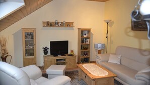 Ein Wohnzimmer mit Fernseher, zwei Sofas, einem Couchtisch und Holzregalen mit verschiedenen Gegenständen.
