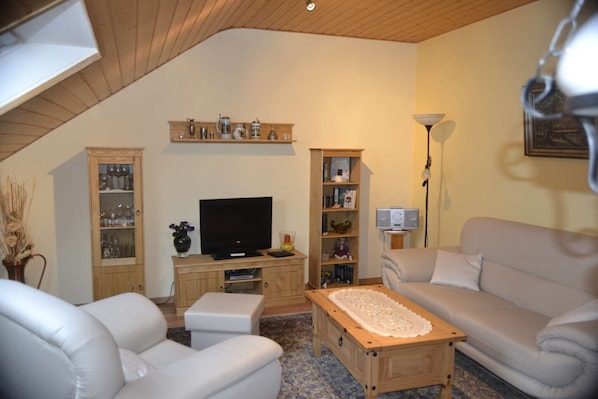 A living room with a television, two sofas, a coffee table, and wooden shelves with various items.