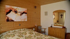 A bedroom with a wooden headboard, a bed with a floral bedspread, a wooden dresser, a chair, a mirror, and a wall-mounted painting. - Apartment 'Haus Moser - Fewo 1' with Valley View, Shared Terrace and Wi-Fi (Eschau)