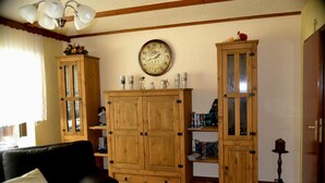 A living room with a black sofa, wooden cabinets, a wall clock, and a bookshelf. - Apartment 'Haus Moser - Fewo 1' with Valley View, Shared Terrace and Wi-Fi (Eschau)