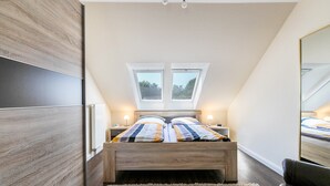 A bedroom with a skylight, a bed with striped bedding, a nightstand, a mirror, and a fluffy rug. - Apartment 'Ferienwohnung  Mühlenweide' with Shared Terrace, Wi-Fi and Air Conditioning (Süderdeich)