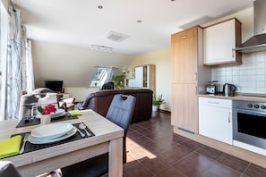 A modern kitchen with a dining area, including a table set for two, a sofa, and a TV.